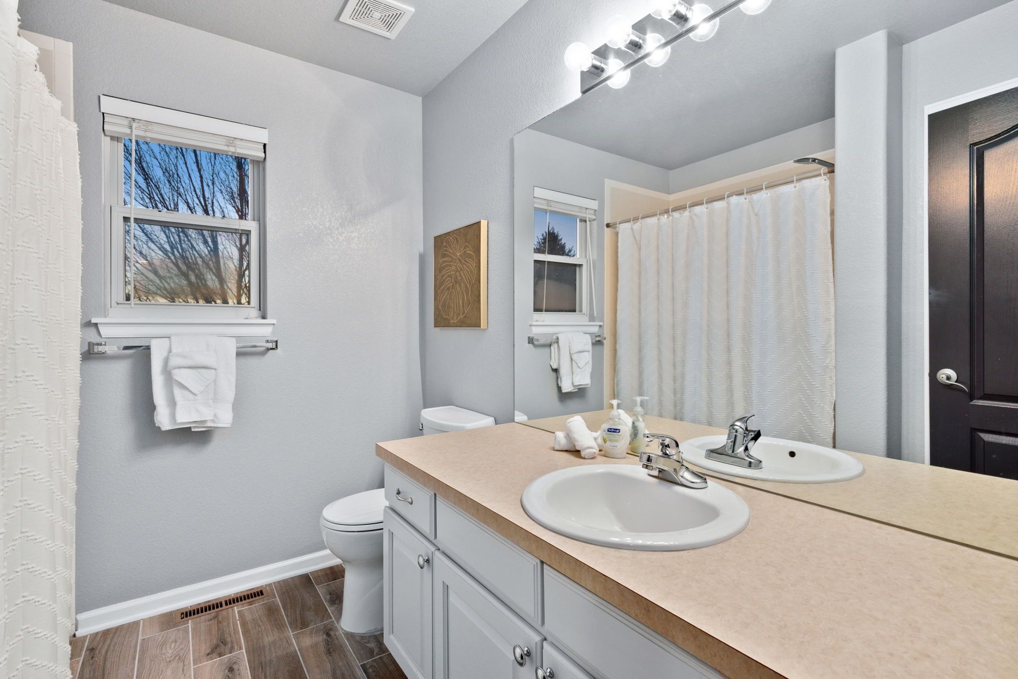 Une salle de bain avec deux lavabos, une fenêtre et un rideau de douche.