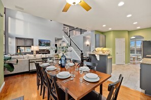 Enjoy meals with family and friends in this dining area, featuring a wooden table and chairs, a staircase, and a kitchen in the background.