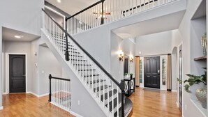 A spacious interior with a central staircase, a dark door, and a light-colored wall. - Spacious Home W/ Fun Amenities | Lake & Mtn Views (Loveland)