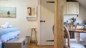 Un dormitorio acogedor con una cama, un taburete pequeño, un cofre de madera y un cuadro en la pared.