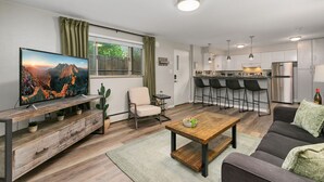 Een moderne woonkamer met een televisie, bank, salontafel en een eethoek met barkrukken.