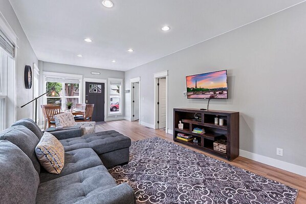 A modern living room with a sectional sofa, a patterned rug, and a TV on a wooden stand.