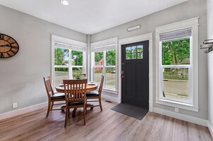 A dining area with a wooden table and chairs, a black door, and large windows with blinds.
