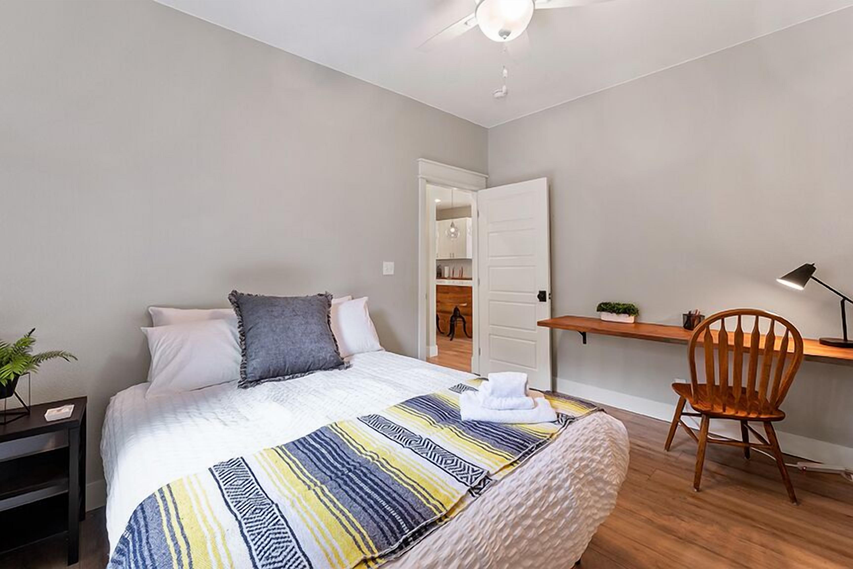 A bedroom with a bed, a desk, a chair, and a ceiling fan.