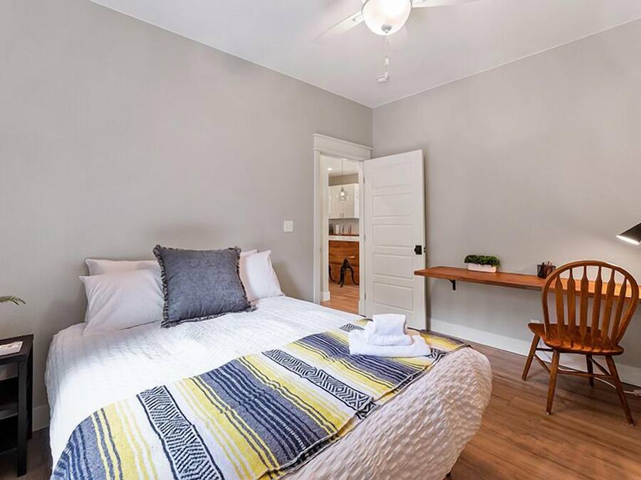 A bedroom with a bed, a desk, a chair, and a ceiling fan.