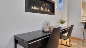 A modern dining area with a black table, two chairs, a glass candle holder, and a framed fireplace. - Sleek Home Near Old Town W/ Rftp Hot Tub & Mtn Views (Fort Collins)