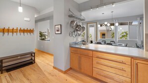 A modern kitchen with wooden cabinets, a large island, hanging pots, and a pendant light. - Sleek Home Near Old Town W/ Rftp Hot Tub & Mtn Views (Fort Collins)