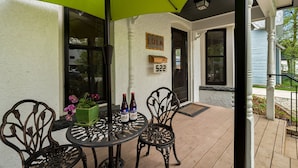 A covered patio with a table and chairs, a green umbrella, and a door with a mailbox. - Lola House! Cozy Comfort, Prime Old Town Location (Fort Collins)