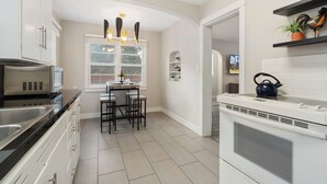 A modern kitchen with white cabinetry, a dining area with a table and chairs, and a built-in oven. - Beautiful Bungalow Next to Csu - Free Cruiser Bikes (Fort Collins)