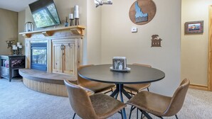 Un coin repas comprenant une table ronde et quatre chaises, un téléviseur à écran plat fixé au-dessus de la table, un meuble en bois doté d’un banc intégré et un luminaire fixé au mur.