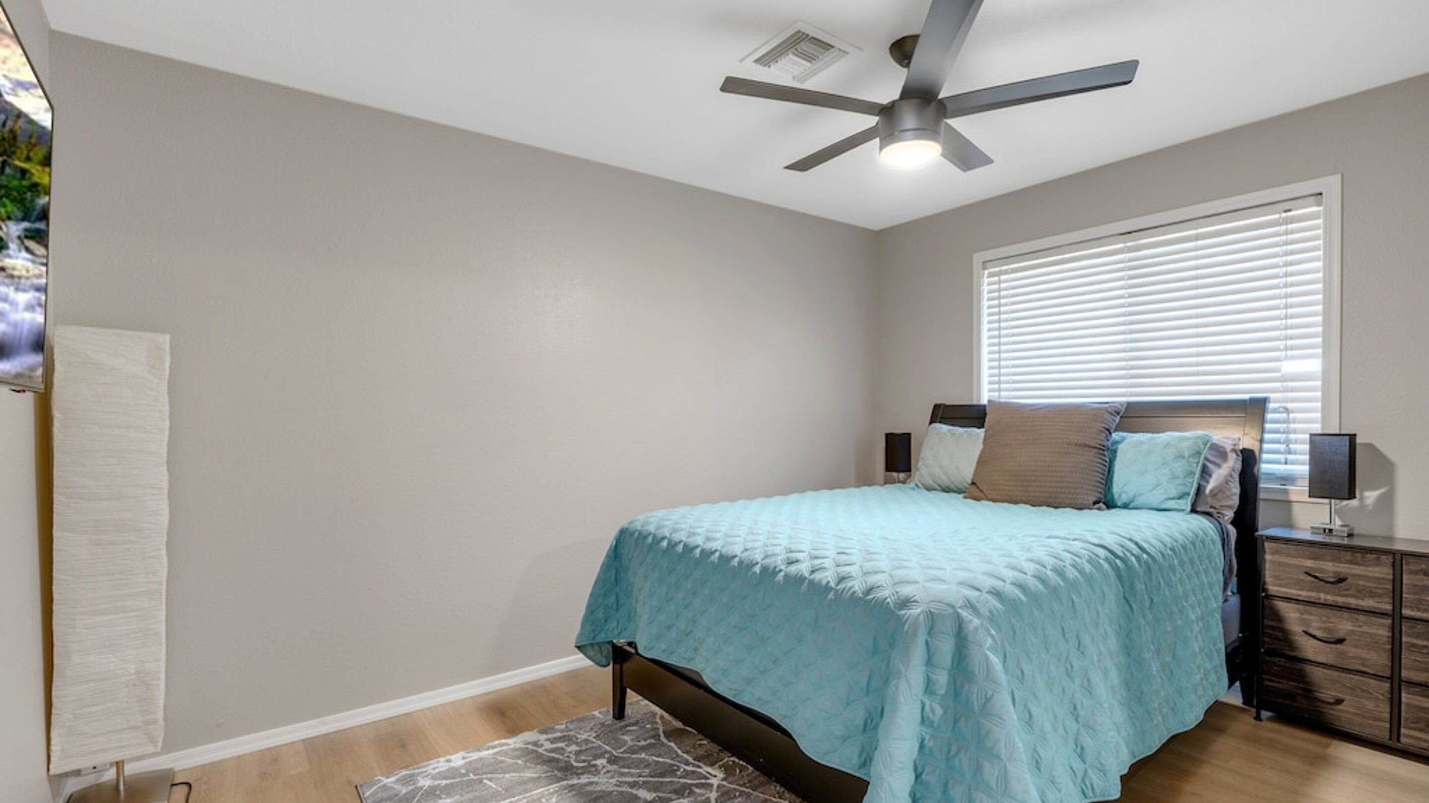 A bedroom with a bed, a nightstand, a ceiling fan, and a window with blinds.
