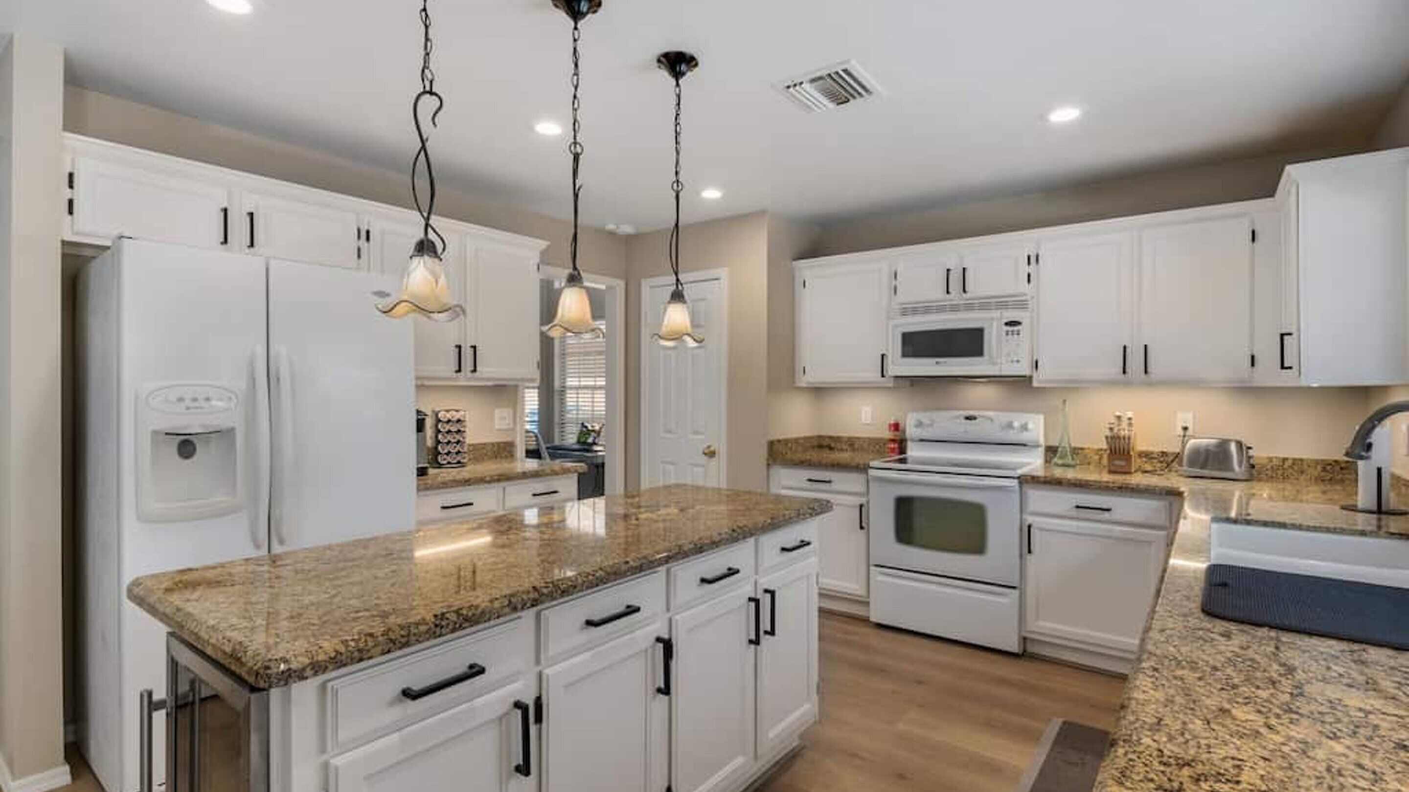 A modern kitchen with white cabinets, granite countertops, stainless steel appliances, and pendant lighting.