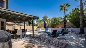 Ein überdachter Patio-Bereich mit Pool, Liegestühlen und Grill.