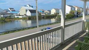 A wooden deck with a railing overlooking a calm body of water, houses in the background, and a clear sky. - 4 BR, 3 bath Cherry Grove Retreat near CG Pier, Private Pool, 1 block to beach (North Myrtle Beach)