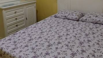 Una habitación con cama, cómoda, aire acondicionado y ventana con barrotes.