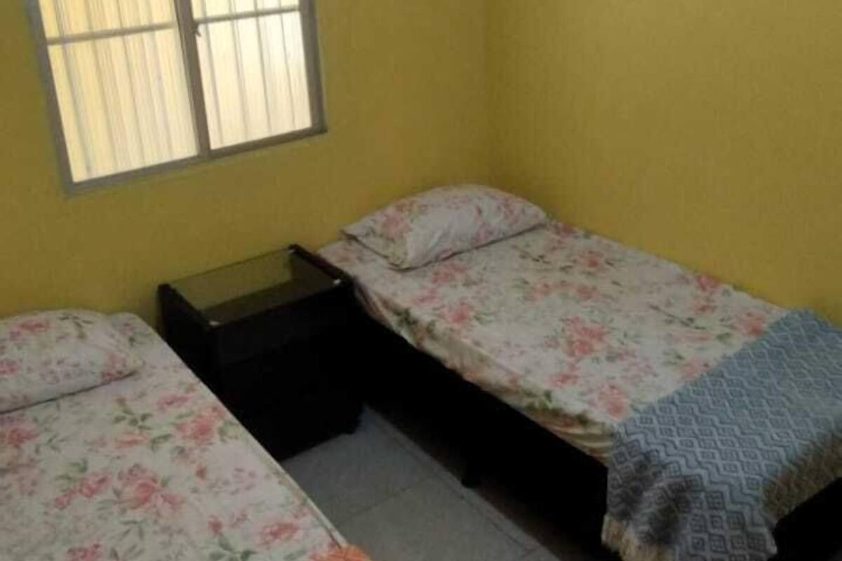 Ein Zimmer mit zwei Einzelbetten, einem Fenster mit Jalousien und einer Deckenleuchte.