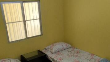 A room with two beds, a window with blinds, a nightstand, and a ceiling light.