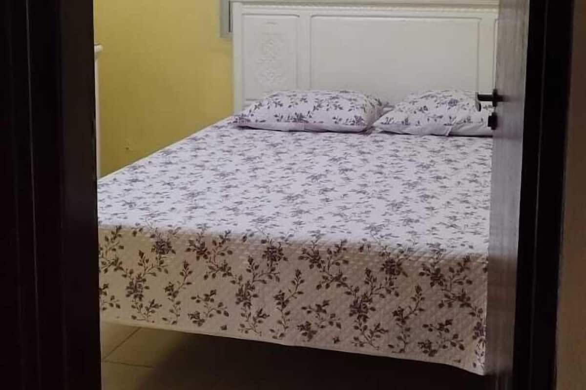 Ein Zimmer mit einem Bett, einem Fenster mit Gitterstäben, einer Klimaanlage und einer Deckenleuchte.
