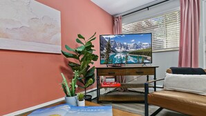 A living room with a television displaying a mountain landscape, a cactus plant, a book titled 'Colorado Atlas', and a sofa.