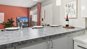A modern kitchen with a marble countertop, a dining area with a table set for two, and a large window with curtains.