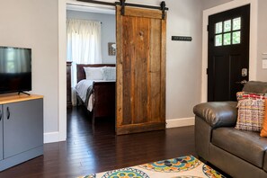 A room with a bed, a television on a cabinet, a sliding barn door, a leather sofa, and a patterned rug.