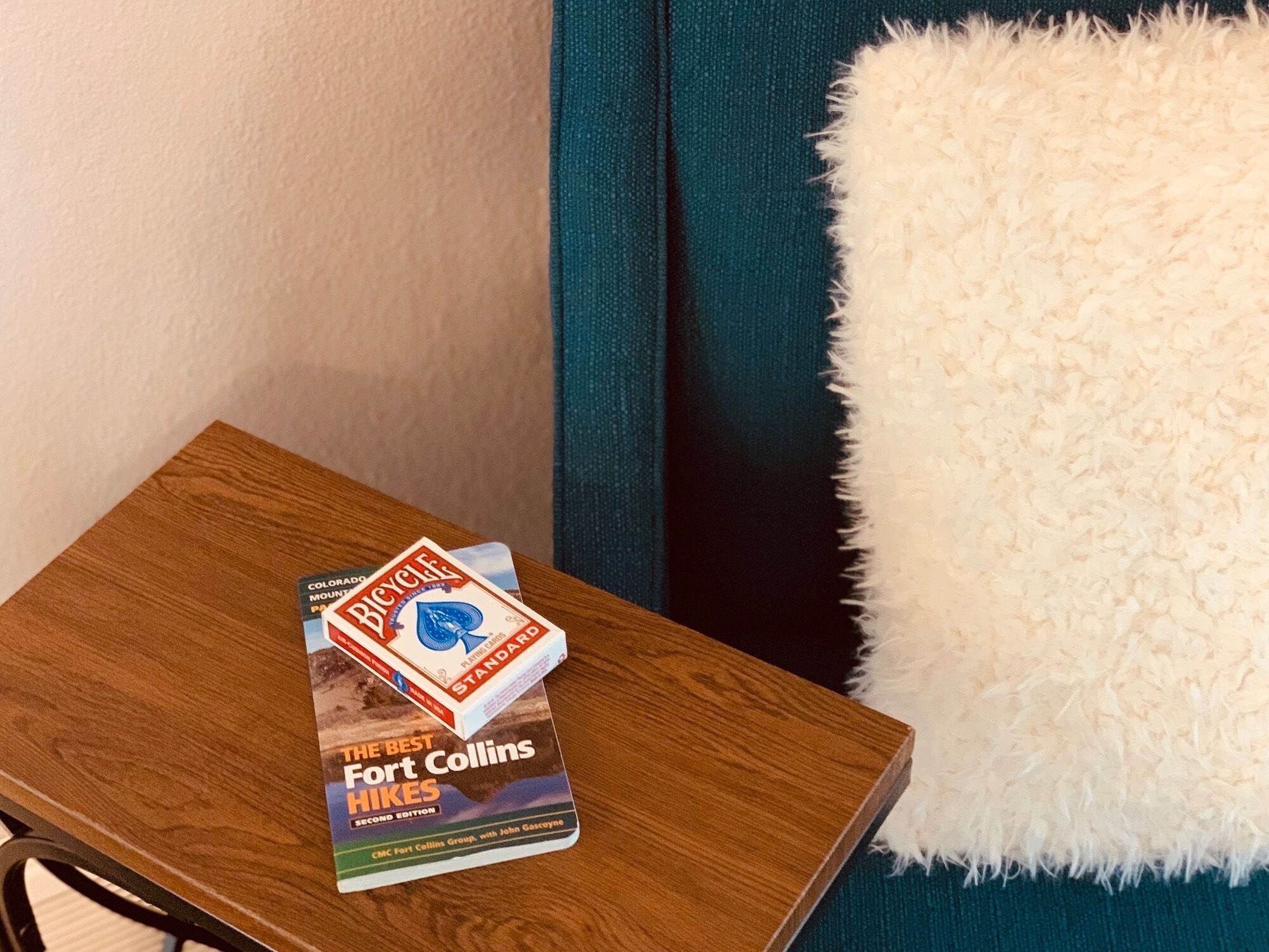 Un livre intitulé « Les plus belles randonnées de Fort Collins » est posé sur une table en bois, à côté d’un coussin blanc et moelleux et d’un rideau vert foncé.