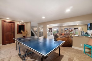 A spacious living area with a ping pong table, a staircase, and a cozy seating area.