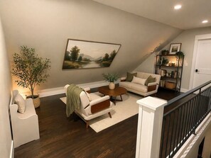 A living room with a sofa, armchair, coffee table, and a painting on the wall.