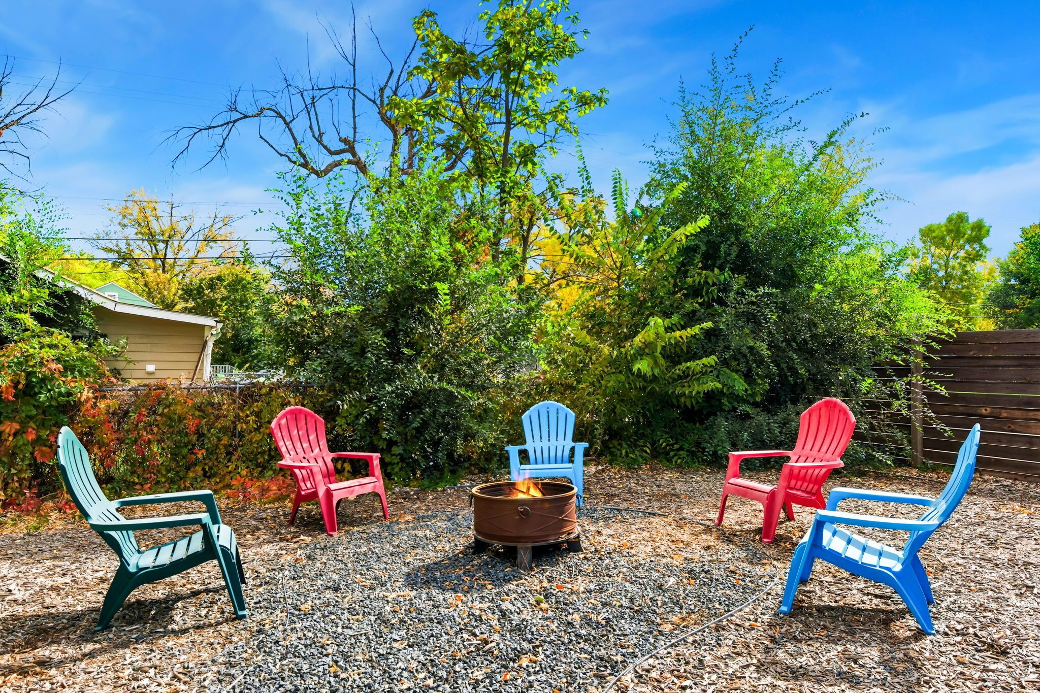 Patio trasero con un brasero rodeado de sillas Adirondack.
