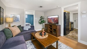 A living room with a sofa, coffee table, and a TV. There is a kitchen visible in the background. - Inviting Bungalow Next to Unc - Free Cruiser Bikes! (Greeley)