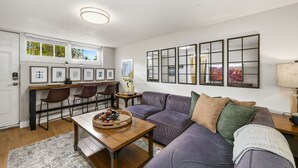 A modern living room with a sofa, a dining table, and a kitchen area with bar stools. - Inviting Bungalow Next to Unc - Free Cruiser Bikes! (Greeley)