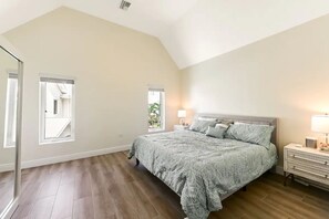 A bedroom with a large bed, a nightstand, a dresser, and two windows.