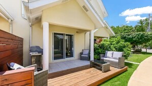 Een overdekt terras met een houten terras, tuinmeubilair en een schuifdeur naar een kamer.