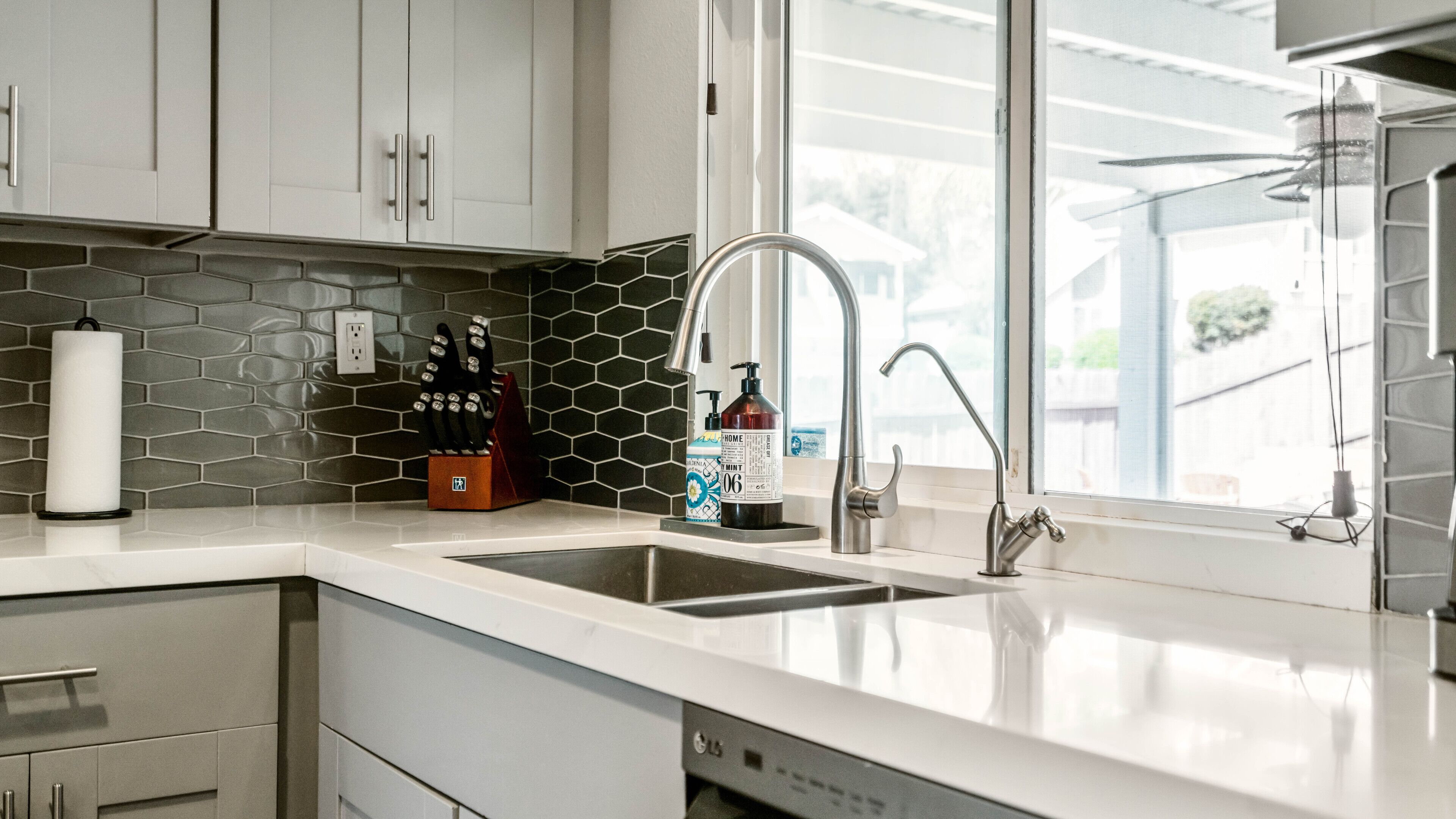 A modern kitchen with white cabinets, a stainless steel sink, and a window with a view of the outside.