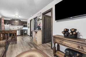 A kitchen with wooden cabinets, a dining area with stools, a TV mounted on the wall, and a cozy seating area with a rug.