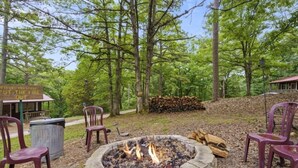 A fire pit surrounded by stone seating, a sign instructing to "put the fire out," and a wooden structure in the background. - Charming Rustic Retreat - Hot Tub - Pool - Coffee - Fire Pit - 1 mile from SDC! (Branson)