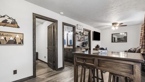 A modern kitchen with wooden flooring, a bar area, and a dining table. - Charming Rustic Retreat - Hot Tub - Pool - Coffee - Fire Pit - 1 mile from SDC! (Branson)