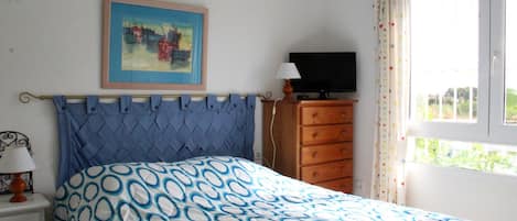 A bedroom with a bed, a dresser, a television, and a painting on the wall.