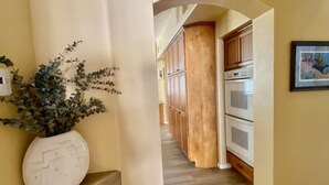 A hallway with wooden flooring, a white vase with a plant, wooden cabinets, and a framed picture on the wall.
