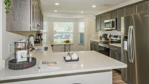 A modern kitchen with stainless steel appliances, a marble countertop, and a view of the street through large windows. - Trailside Oasis: 3BR Pool & Spa – Minutes from Trail, Ocala & Crystal River (Inverness)