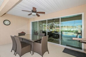 Un patio couvert avec une porte vitrée donnant sur une piscine, un ventilateur de plafond et une horloge murale.