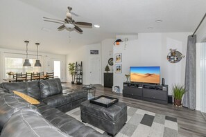 A modern living room with a leather sofa, a flat-screen TV, and a ceiling fan.