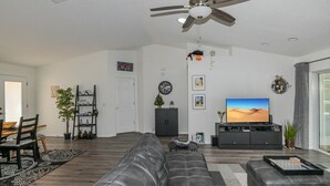 A modern living room with a leather sofa, a dining area with chairs, a TV, and a ceiling fan. - Trailside Oasis: 3BR Pool & Spa – Minutes from Trail, Ocala & Crystal River (Inverness)