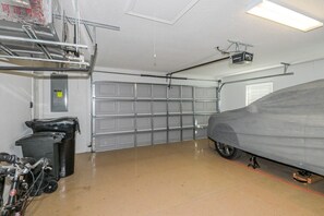 A garage with a car covered in a grey tarp, a bicycle, and a trash bin.