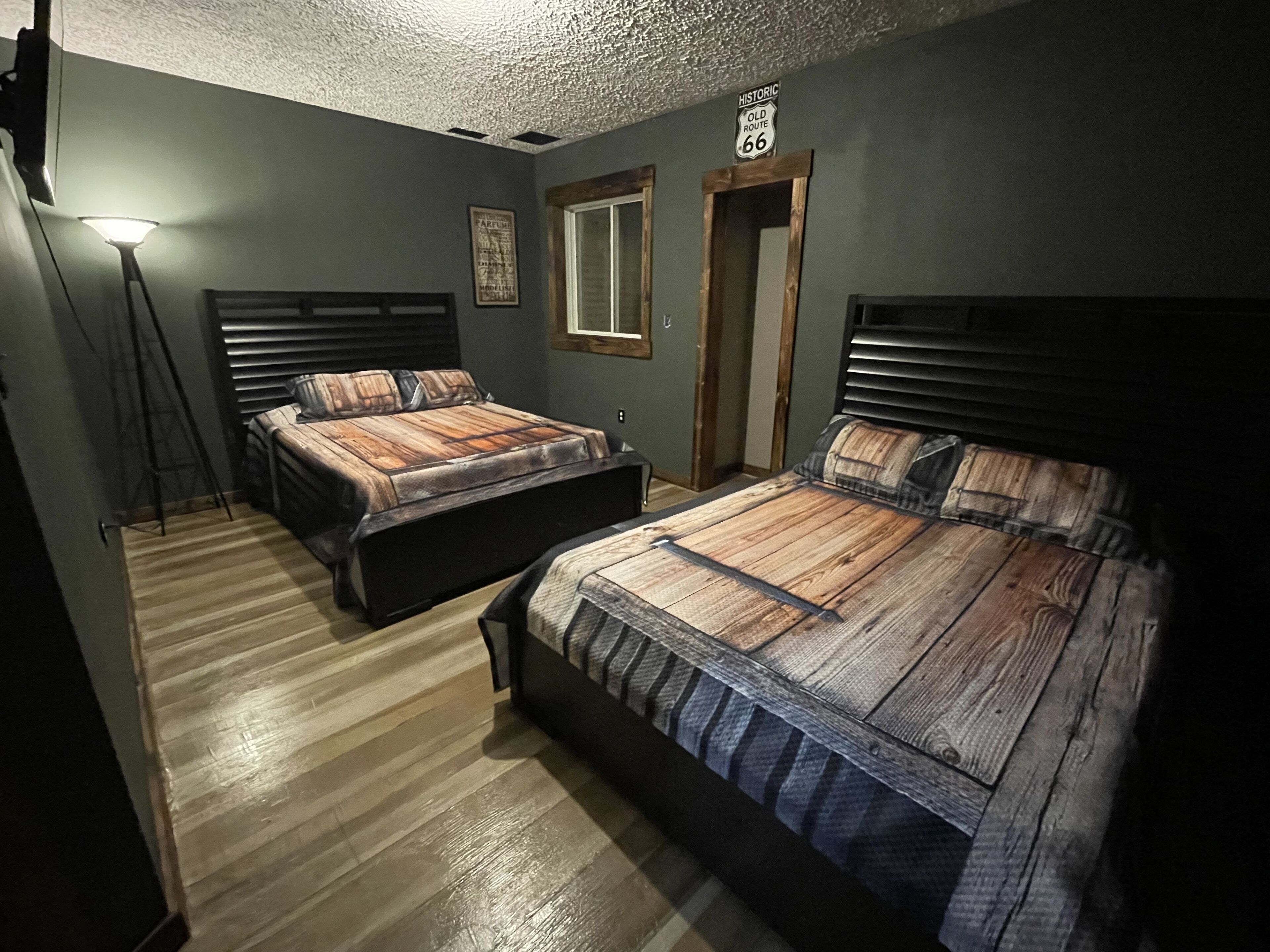 A bedroom with two beds, a wooden floor, a mirror, and a 'Historic Old Route 66' sign.