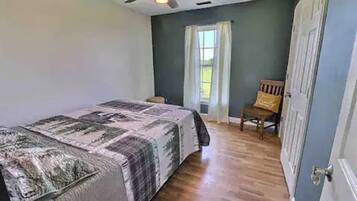Um quarto com uma cama, um ventilador de teto, uma janela com cortinas e uma porta.