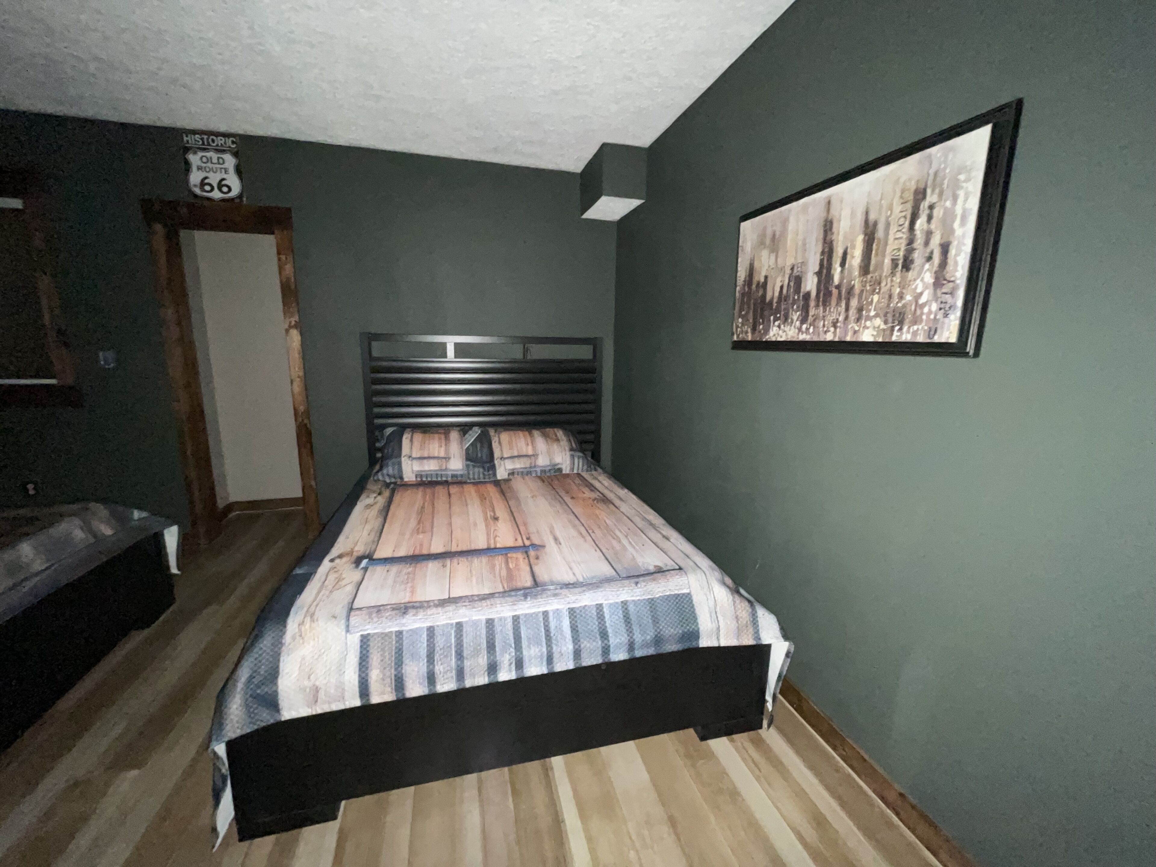 Una camera da letto con un letto, una testiera, una porta, un quadro appeso al muro e un cartello sopra la porta.