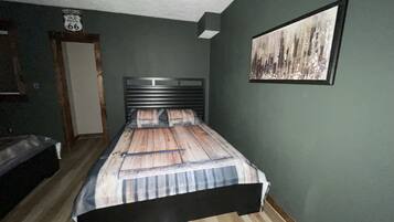 Una camera da letto con un letto, una testiera, una porta, un quadro appeso al muro e un cartello sopra la porta.