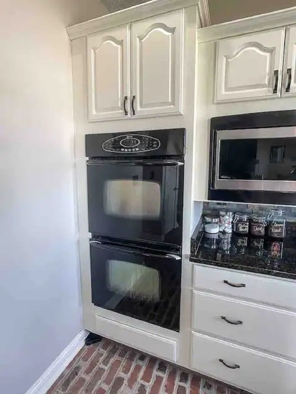Een keuken met witte kastjes, een dubbele oven en een magnetron.