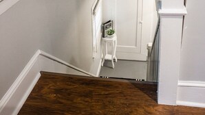 Una scala con un pavimento di legno scuro, pareti bianche e una porta bianca in cima.